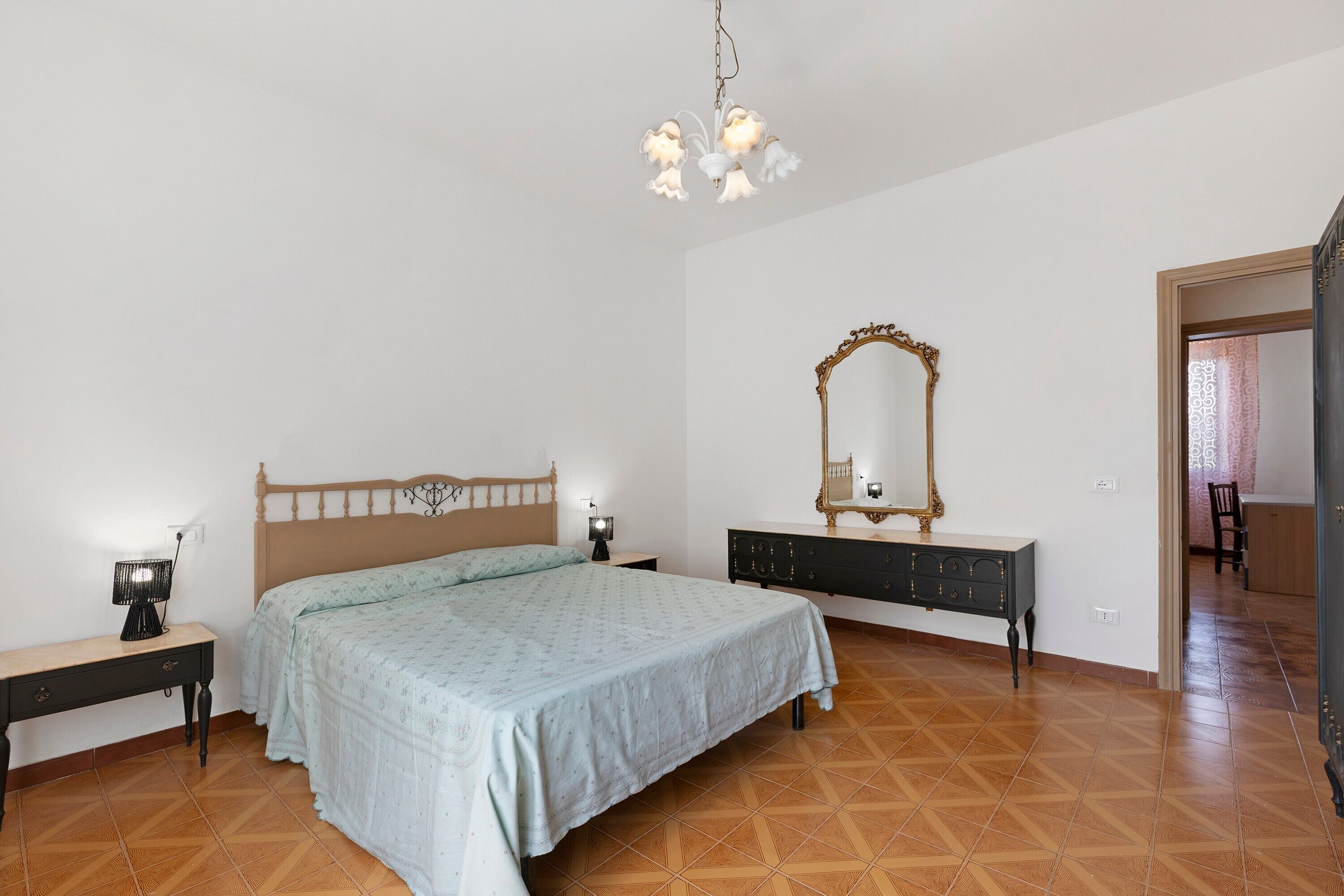 Un dormitorio con cama, mesitas de noche, cómoda, espejo y candelabro.
