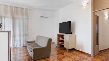 A living room with a sofa, a television on a wooden cabinet, and patterned floor tiles.