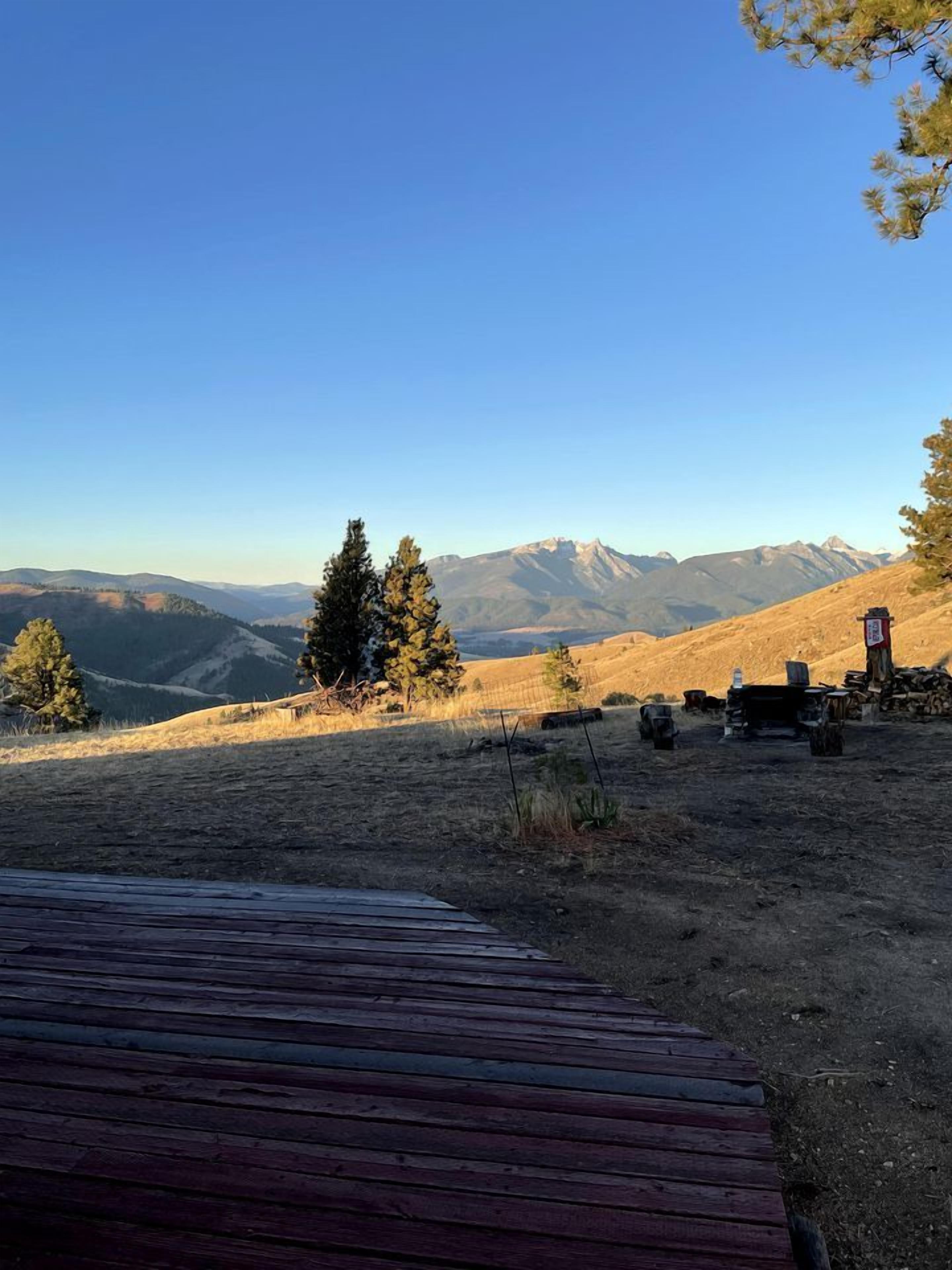 Una terraza de madera con vistas a un paisaje montañoso, árboles y cielo despejado.