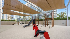 Un parque infantil con un tobogán, columpios y un caballo balancín rojo.