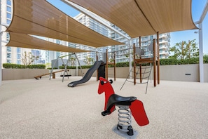 A playground with a slide, swings, and a red rocking horse. - StayShort | Stunning Beachfront 2-Bedroom Apartment Sleeps 6 with Infinity Pool, Skyline Views & Private Beach Access (Dubai)