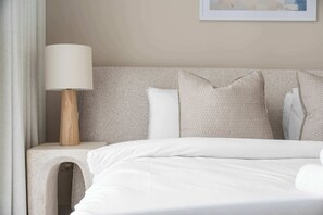 A neatly made bed with white linens, a wooden bedside table with a lamp, and a headboard with multiple pillows. - StayShort | Stunning Beachfront 2-Bedroom Apartment Sleeps 6 with Infinity Pool, Skyline Views & Private Beach Access (Dubai)