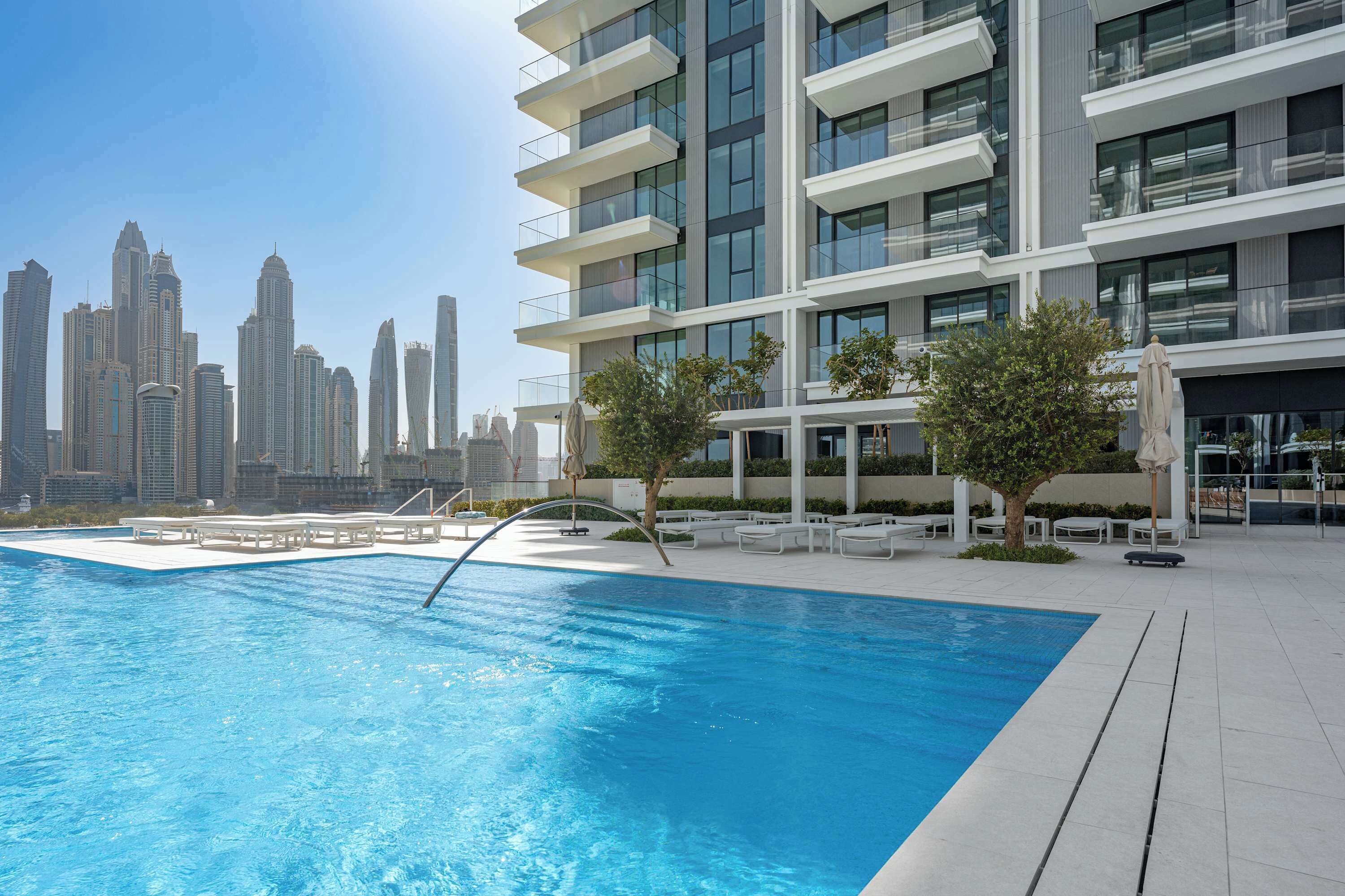 A modern hotel with a swimming pool, outdoor seating, and a view of the city skyline.