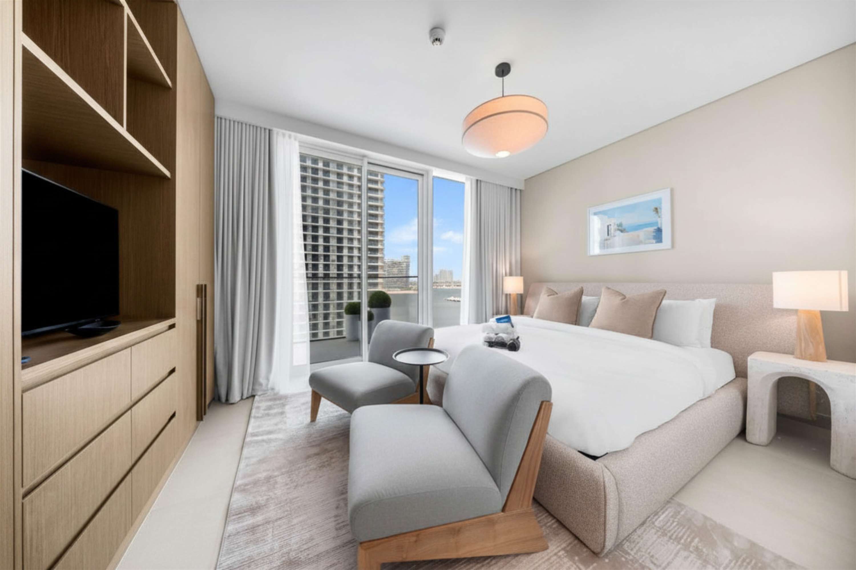 A modern hotel room with a large bed, a television, a seating area, and a balcony with a city view.