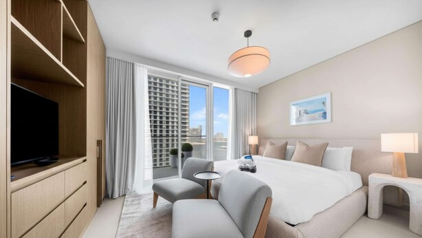 Una habitación de hotel moderna con una cama grande, televisión, zona de estar y balcón con vistas a la ciudad.