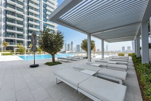 A rooftop lounge area with sunbeds, a pool, and a view of the city skyline. - StayShort | Stunning Beachfront 2-Bedroom Apartment Sleeps 6 with Infinity Pool, Skyline Views & Private Beach Access (Dubai)