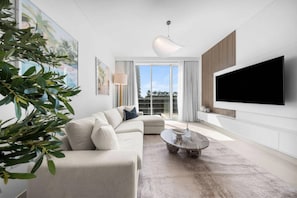 A modern living room with a sectional sofa, a coffee table, and a flat-screen TV mounted on the wall. - StayShort | Stunning Beachfront 2-Bedroom Apartment Sleeps 6 with Infinity Pool, Skyline Views & Private Beach Access (Dubai)