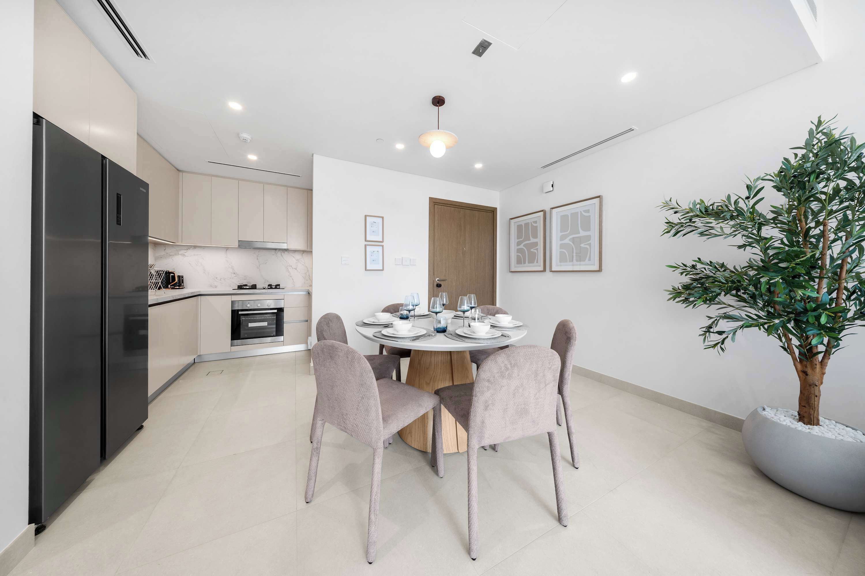 A modern kitchen with a built-in oven, a refrigerator, and a dining area with a round table and four chairs.