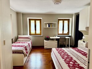 A bedroom with two beds, a desk, a chair, a bookshelf, and a window with curtains. - Dolomiti Cadore Home, in the heart of the Cadore Dolomites, 5 minutes from Sappada (san pietro di cadore)