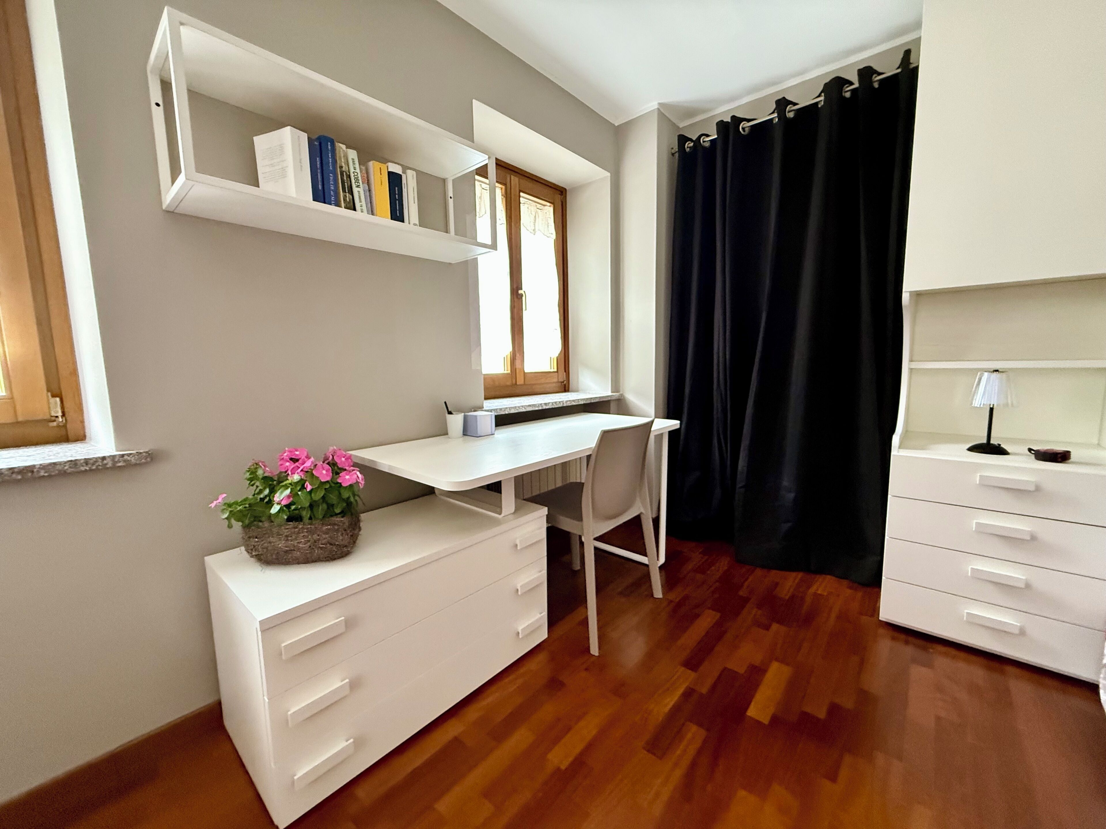 A room with a desk, a chair, a bookshelf, a dresser, and a window with curtains.