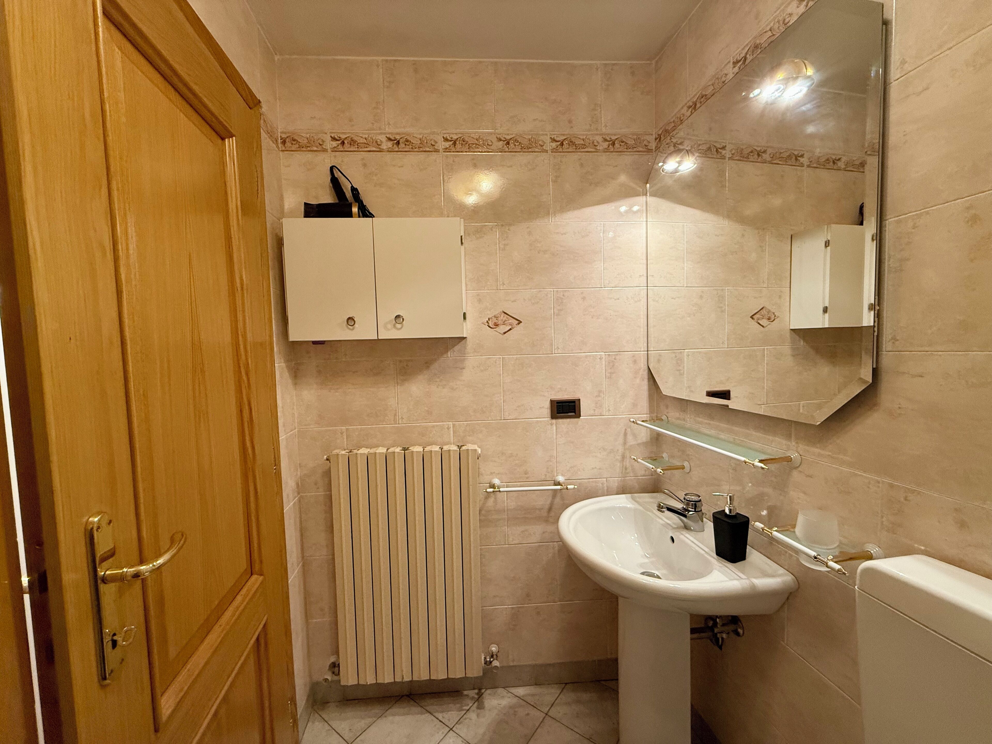 A bathroom with a wooden door, a radiator, a sink, and a mirror.