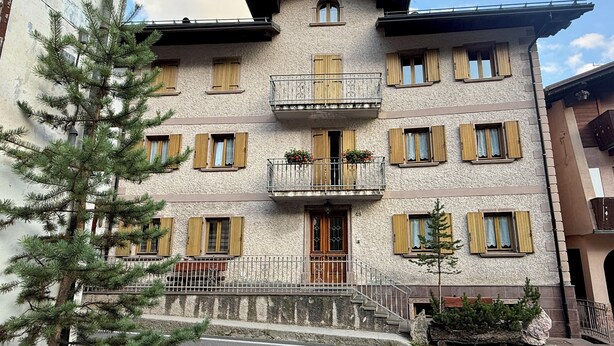 Ein mehrstöckiges Gebäude mit Balkon, Holzhinterfenstern und einer Steinfassade.