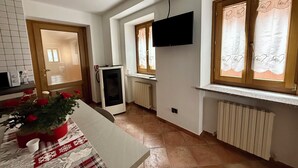 Eine Küche mit Tisch, Kühlschrank, Wandfernseher und einem Fenster mit Vorhängen.