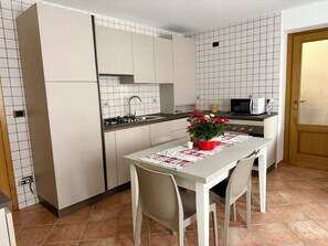 A compact kitchen with white cabinets, a tiled backsplash, a dining table with chairs, and a microwave. - Dolomiti Cadore Home, in the heart of the Cadore Dolomites, 5 minutes from Sappada (san pietro di cadore)