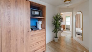 Ein Flur mit einem Holzschrank, einem Topfpflanzen, einem Spiegel und einem Blick in ein Schlafzimmer mit Bett und Fenster.