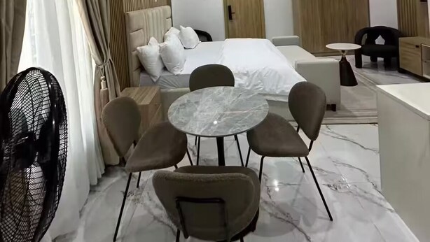 Hotelkamer met een bed, een rond marmeren tafeltje met stoelen, een zwarte ventilator en een klein nachtkastje.
