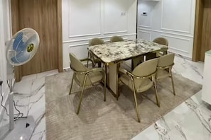 A conference room with a marble-topped table, six chairs, a standing fan, and a marble floor. - Luxury Apartment, 2 Bedrooms, Kitchenette, Courtyard View (Lagos)
