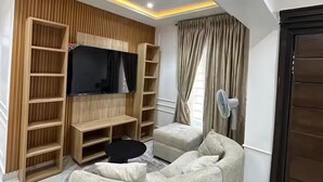 Een woonkamer met een televisie, houten planken, een ventilator en een bank.