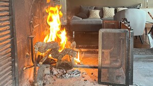 A fireplace with burning logs, a sofa, and a table in a room with a wooden ceiling. - Oustal Fraïssignol, a comfortable guesthouse (Fraisse-sur-Agout)