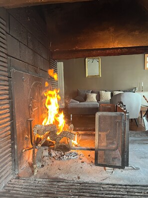 Ein Kamin mit brennendem Holz, ein Sofa und ein Tisch in einem Raum mit Holzboden.