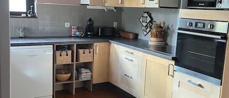 Una cocina con alacenas de madera, un lavavajillas Bosch, un microondas y un reloj en la pared.