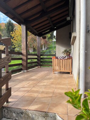 Un patio couvert avec un banc en bois, une plante en pot et une vue sur un paysage verdoyant.