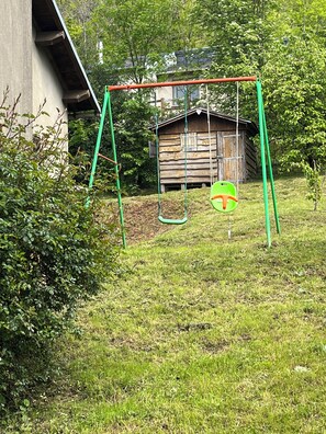 Eine Schaukelanlage in einer grünen Umgebung, im Hintergrund ein Holzgebäude.