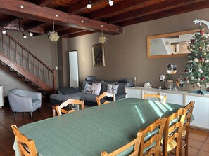 Un coin repas avec une table verte, des chaises en bois, un escalier, un canapé gris et un sapin de Noël.