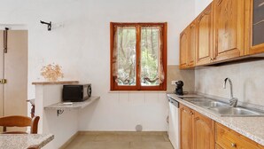 A compact kitchen with wooden cabinets, a built-in microwave, a sink, and a window with curtains. - Apartment 'Terra' with Shared Pool, Garden, and Wi-Fi (Volterra)