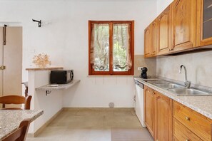 A compact kitchen with wooden cabinets, a built-in microwave, a sink, and a window with curtains. - Apartment 'Terra' with Shared Pool, Garden, and Wi-Fi (Volterra)