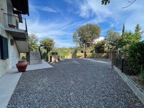 A gravel driveway leading to a building with a balcony, surrounded by trees and a clear sky. - Apartment 'Terra' with Shared Pool, Garden, and Wi-Fi (Volterra)