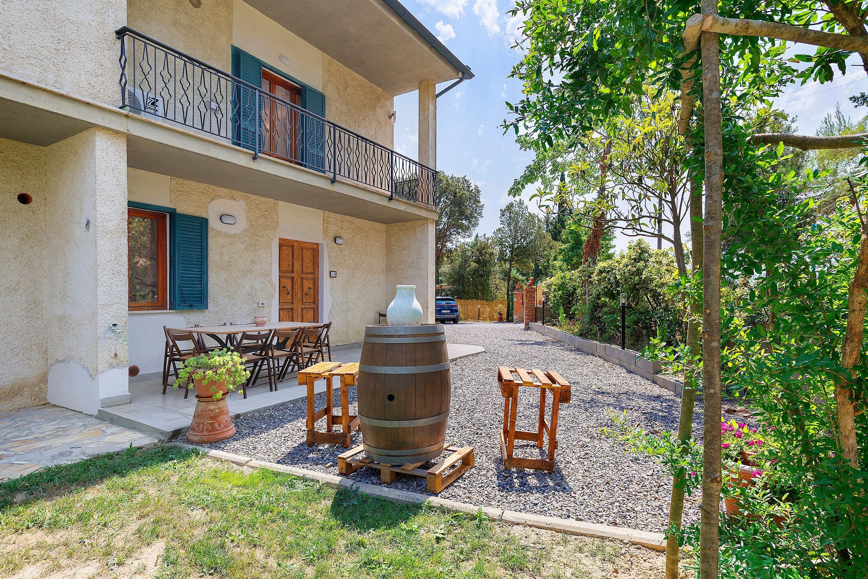 A two-story building with a balcony, a wooden table and chairs, a large barrel, and a gravel driveway.