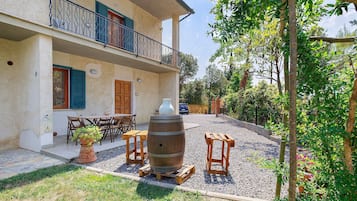 A two-story building with a balcony, a wooden table and chairs, a large barrel, and a gravel driveway.