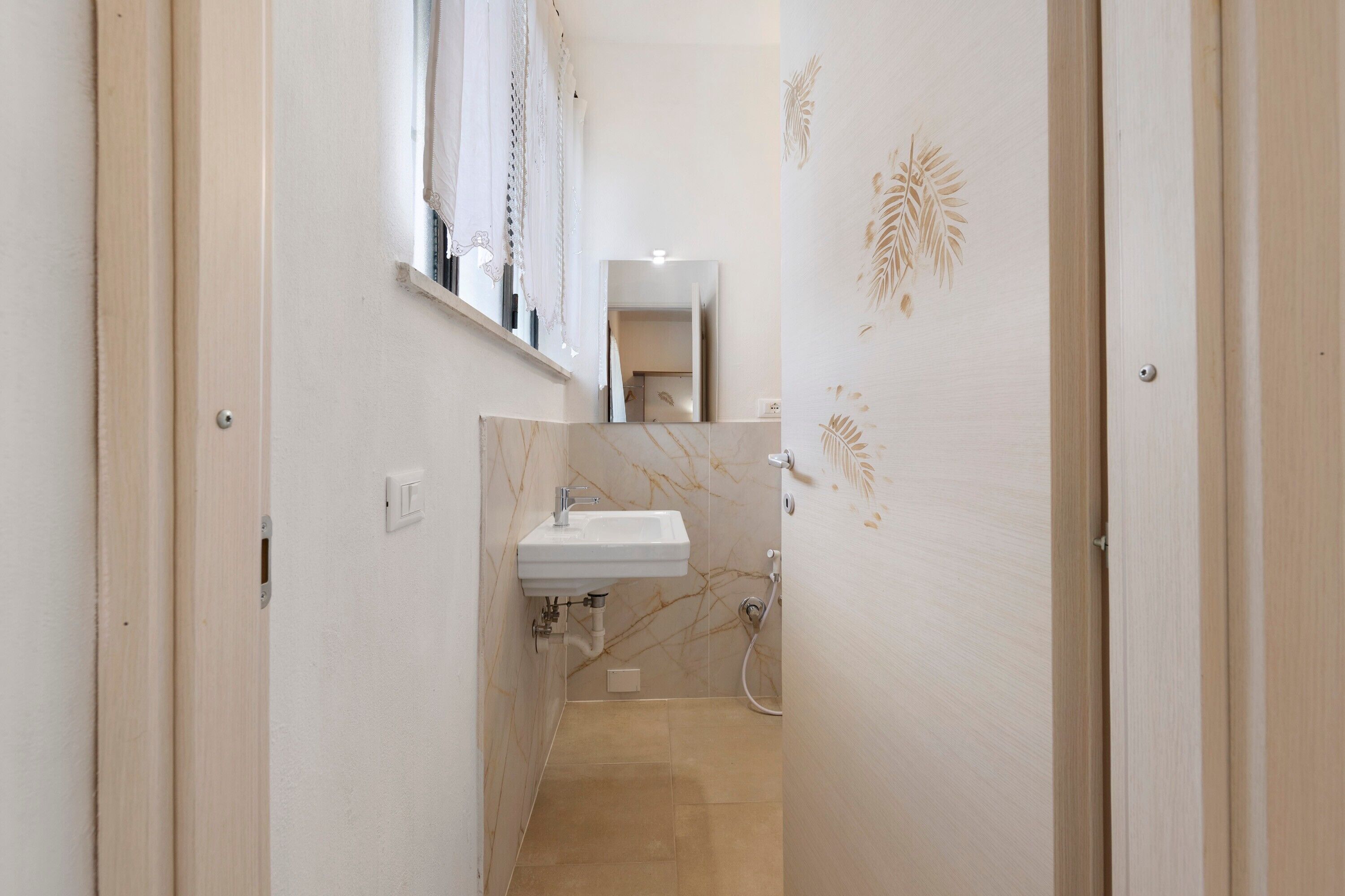 Un couloir étroit mène à une salle de bain équipée d’un lavabo, d’un miroir et d’un porte-serviettes.
