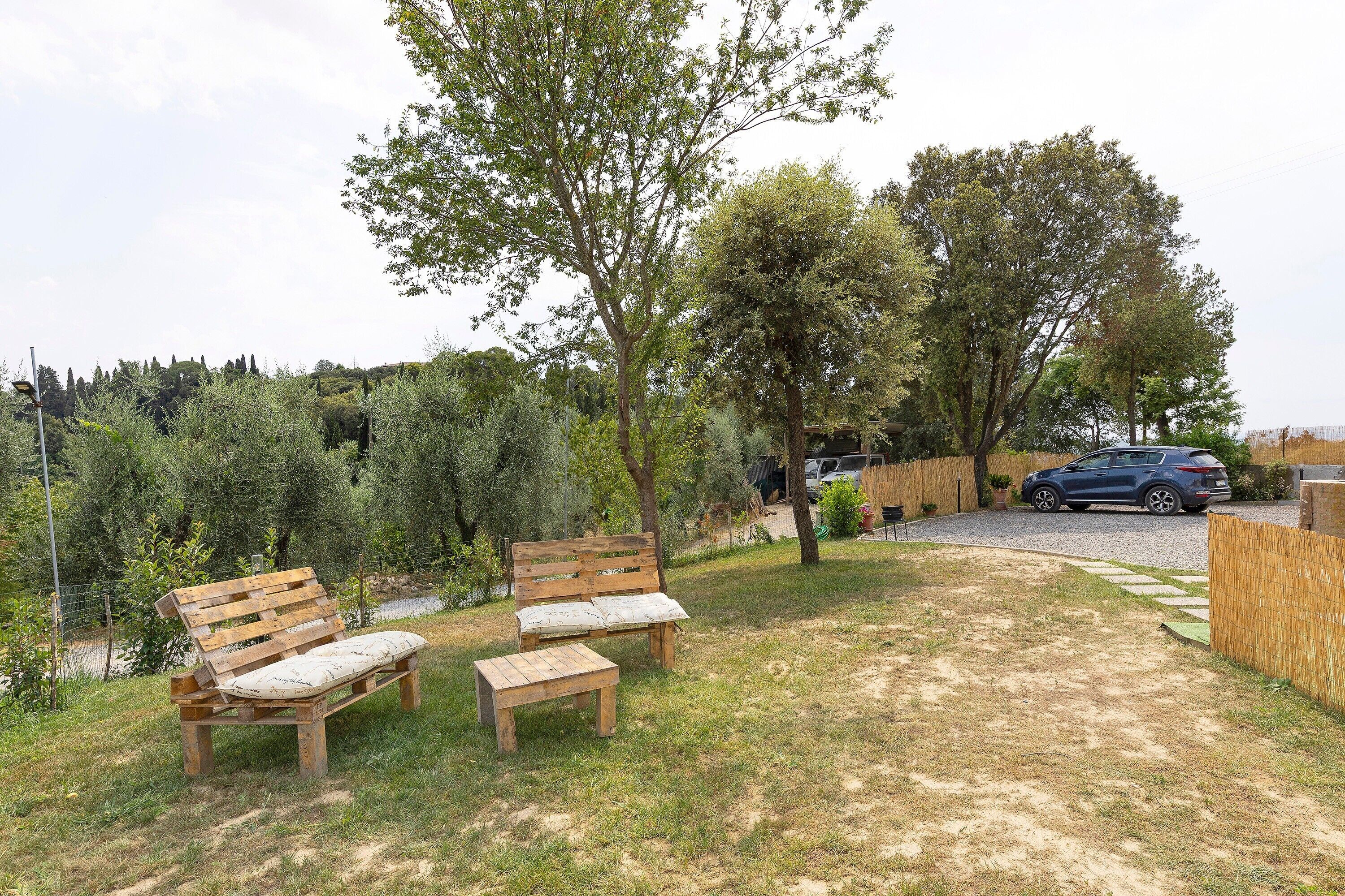 A backyard with a wooden bench, a small table, and a tree. There is a car parked in the background.
