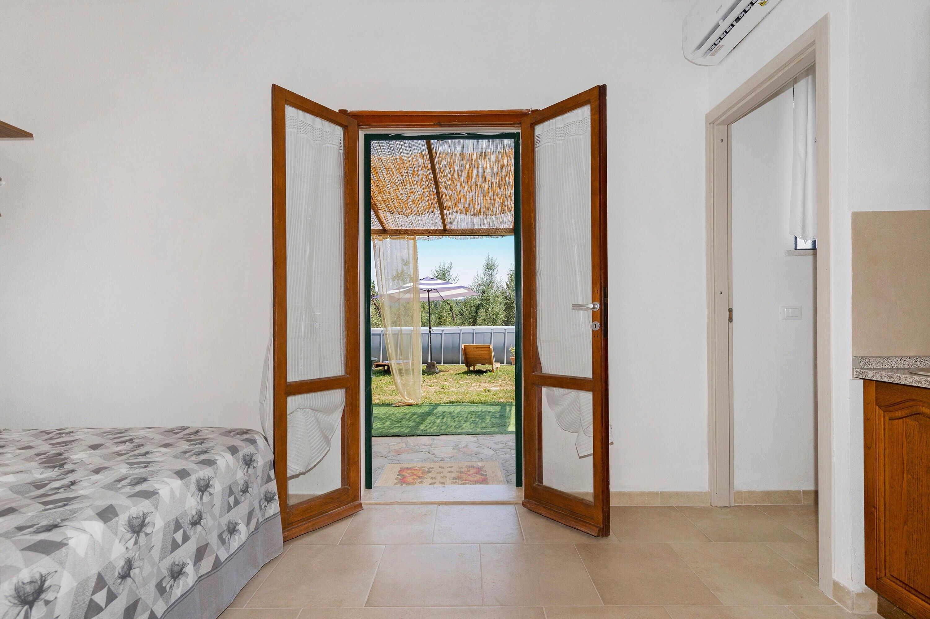 A room with a bed, a door leading outside, and a small kitchenette area.