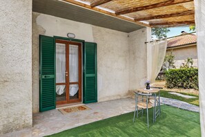 A covered outdoor area with a stone floor, a wooden door with green shutters, and a small table with a chair. - Mini appartamento Terra! - Benvenuti a Villamagna di Volterra! (Volterra)