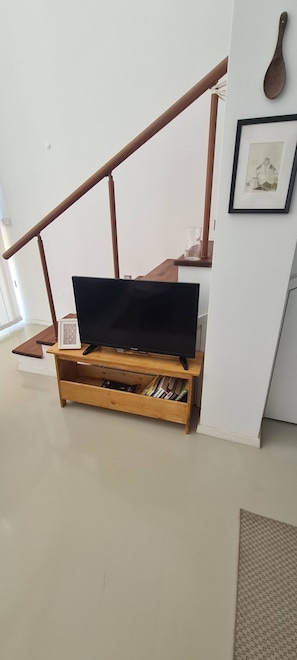 Un moble de televisió de fusta amb un televisor de pantalla plana, un quadre amb marc a la paret i una escala amb barana de fusta.