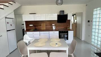 A modern kitchen with white cabinets, a dining table with four chairs, and a hanging light fixture.