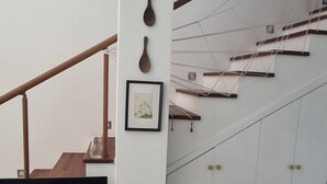 Una sala de estar con un mueble de televisión de madera, un sofá, una escalera con armarios blancos y un marco de fotos colgado en la pared.