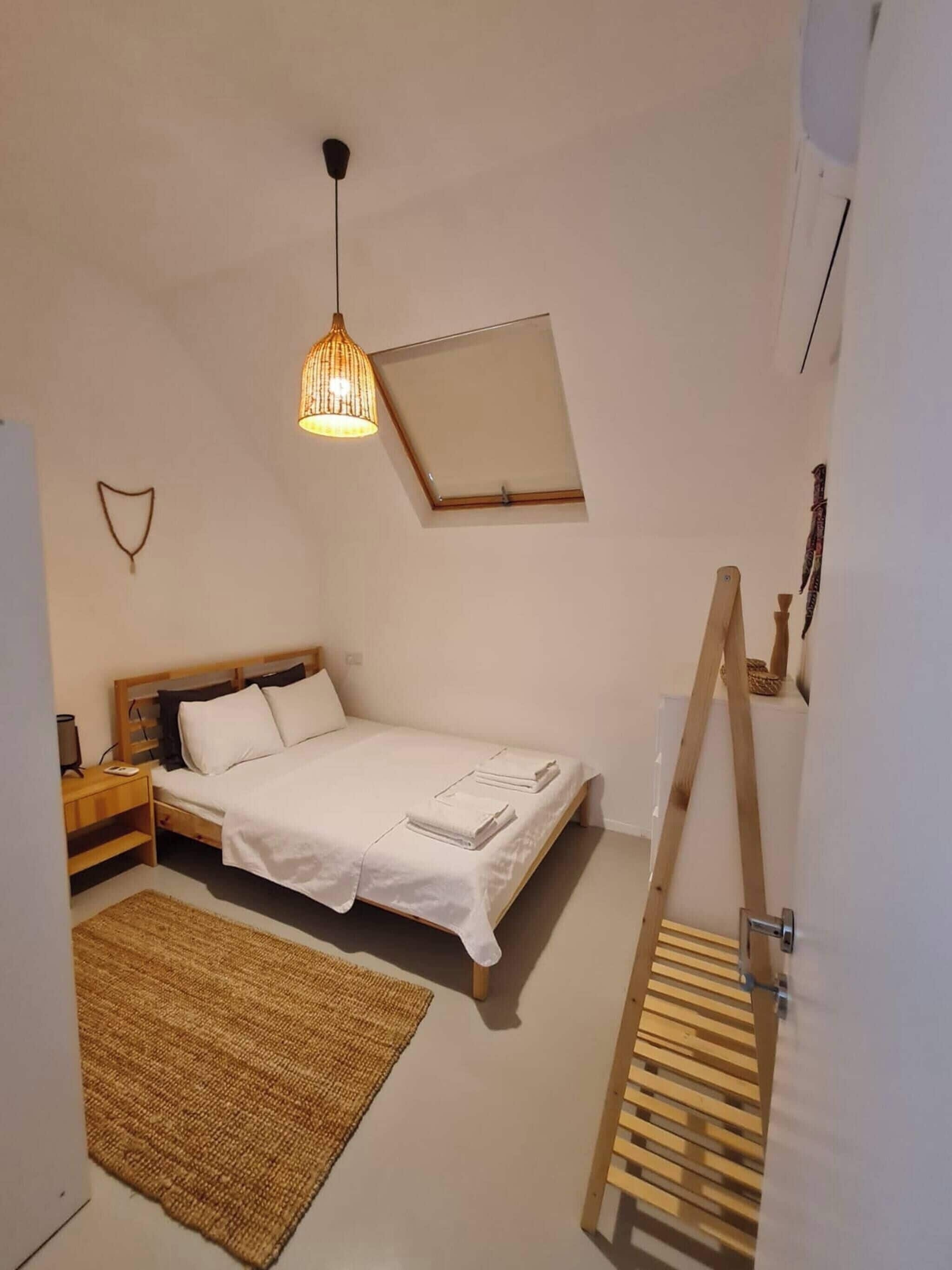 Ein Schlafzimmer mit einem Bett, Nachttisch, Lampe, Teppich und einer Holzleiter.