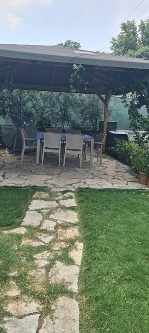A covered patio area with outdoor furniture, a stone pathway, and a grassy lawn.