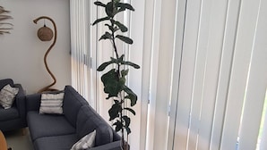 A living room with a grey sofa, a yellow armchair, a potted plant, and white blinds. - Serene 3-bedroom Villa Rental in Köyceğiz, Turkey (Koycegiz)