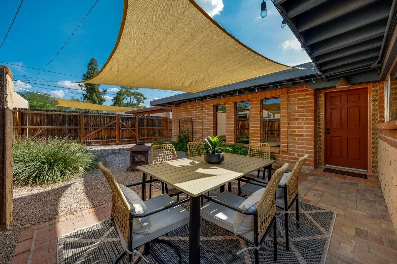 Een terras buiten met een tafel en stoelen, een houten omheining en een bakstenen gebouw op de achtergrond.