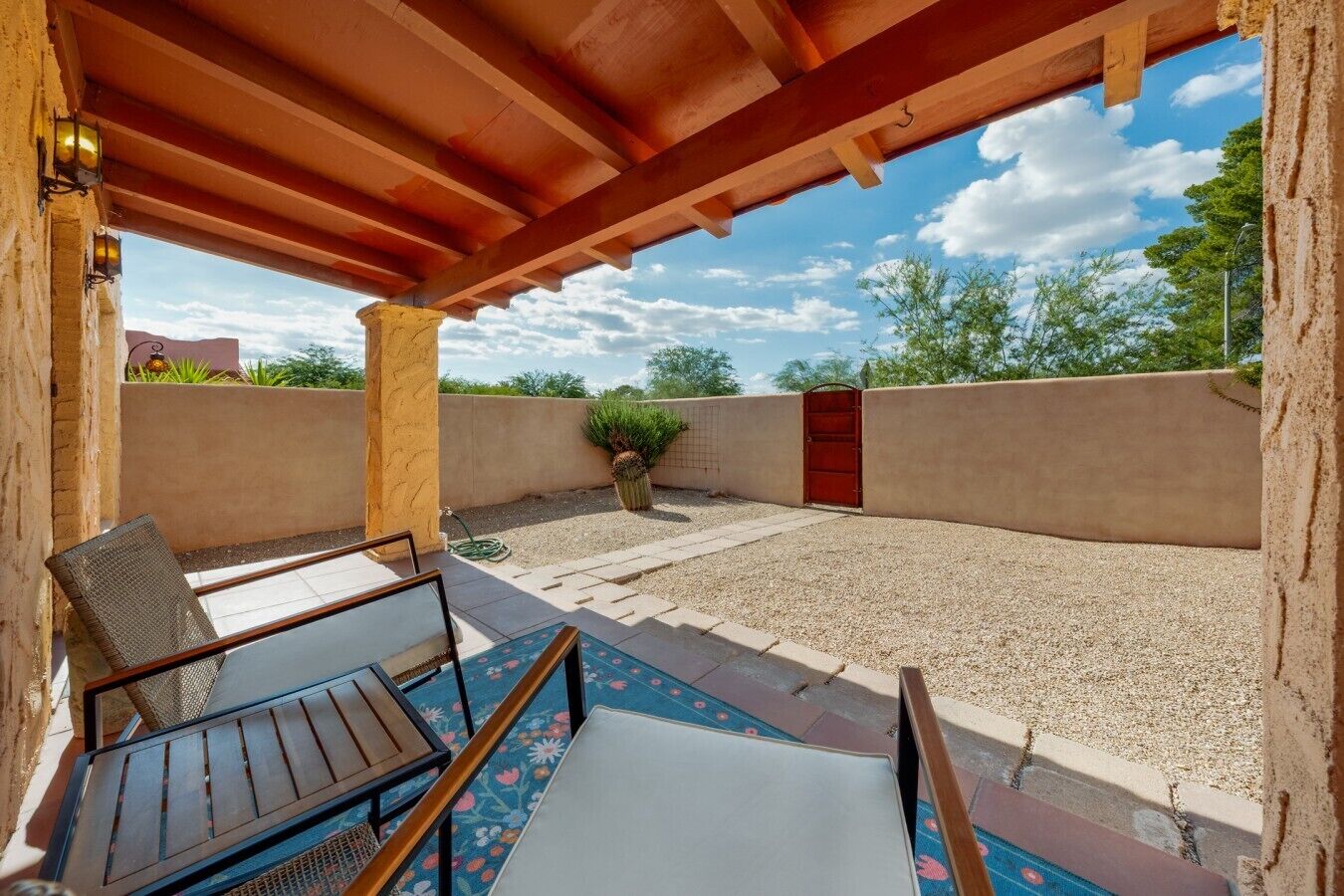 An outdoor patio with a wooden pergola, a seating area with a table and chairs, and a gravel ground.