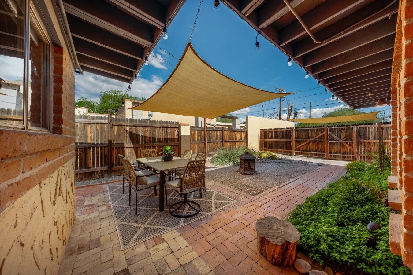 An outdoor patio with a table and chairs, surrounded by a wooden fence and a large shade sail.
