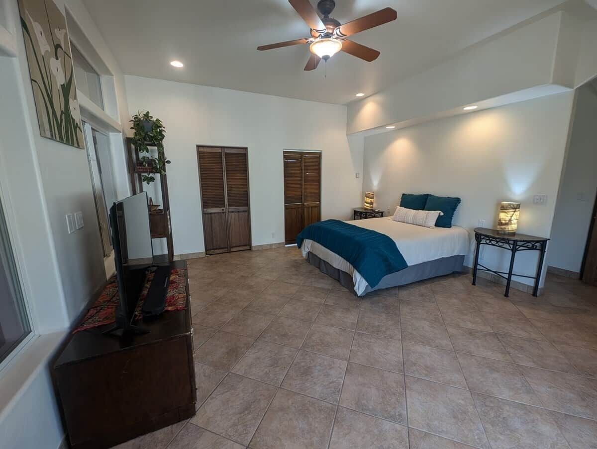 A bedroom with a bed, a television, a ceiling fan, and a small table.