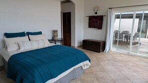 A bedroom with a large bed, a bedside table, a cabinet, and a sliding glass door leading to an outdoor area. - Expansive ranch house w/ guest suite for groups (Cochise County)