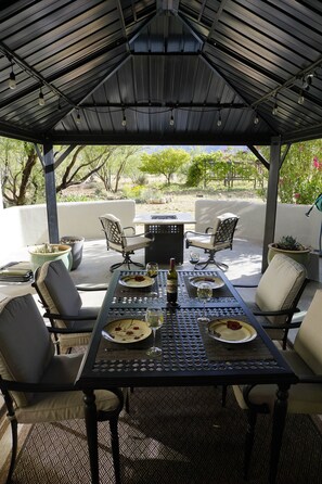 An outdoor patio with a table set for dining, surrounded by chairs, and a pergola overhead. - Expansive ranch house w/ guest suite for groups (Cochise County)