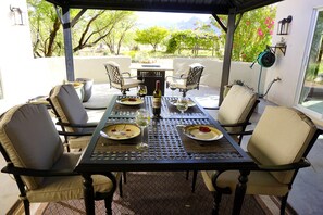 An outdoor patio with a table set for two, surrounded by chairs, and a view of trees and mountains in the background.